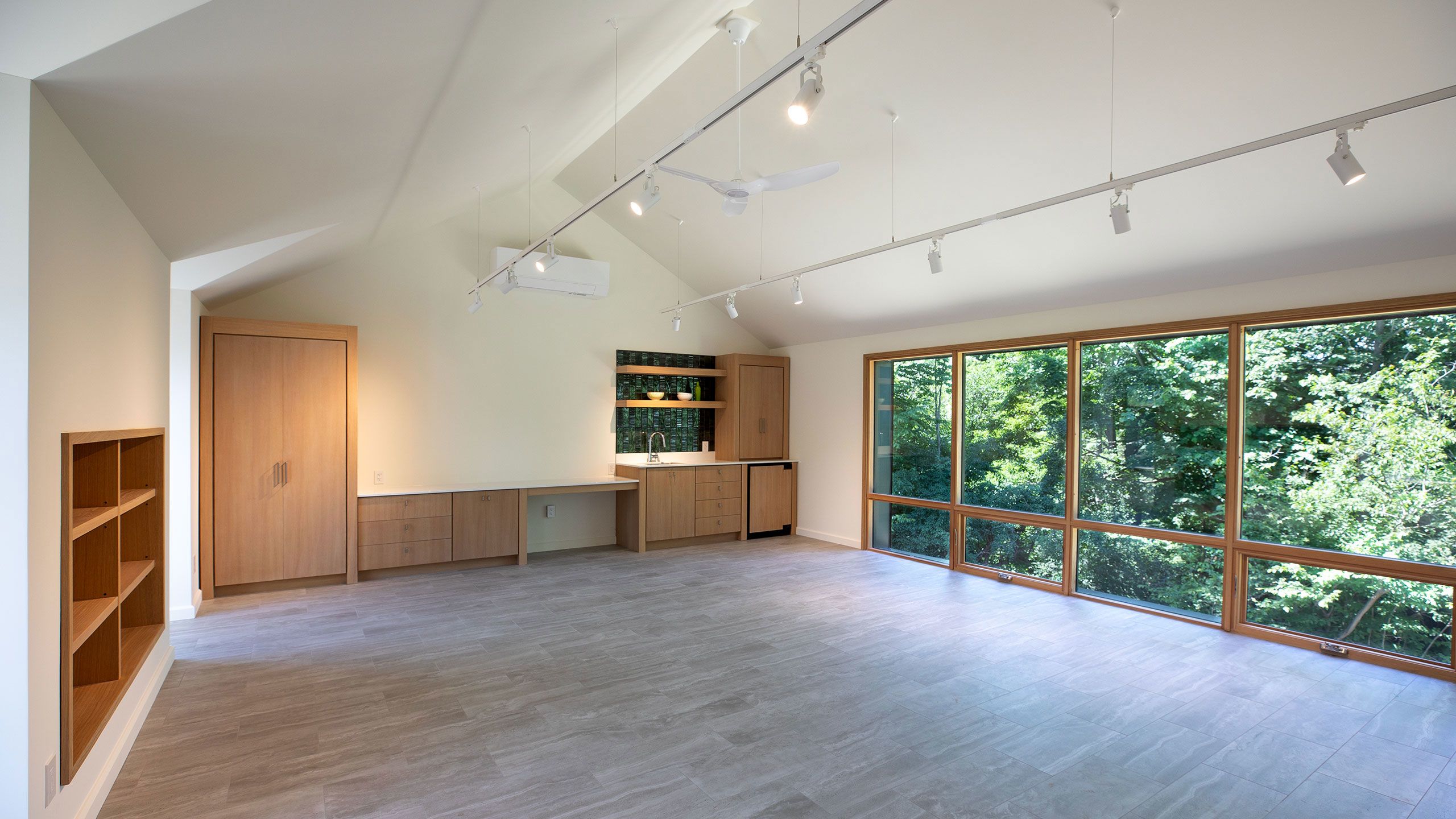 Guest Suite main room with white track lighting, a large wall of windows and a white oak built-in custom kitchen. 