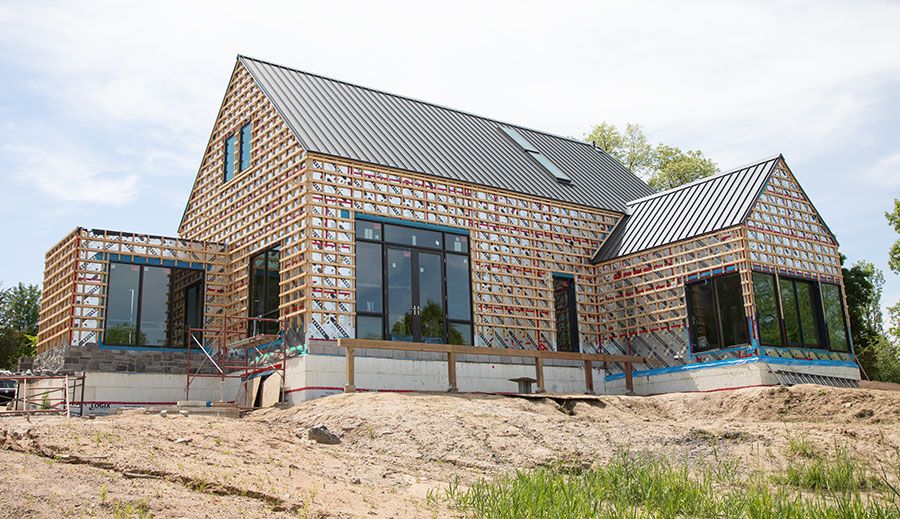 View of the steel roof completed, wood strapping covering the house ready for the application of Maibec siding and foundation ready for the stone application